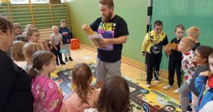 Dzieci grają w wielkoformatową grę planszową „Wygraj bezpieczeństwo”, pokazującą, jak działa grywalizacja w edukacji o zasadach ruchu drogowego.