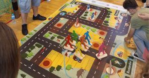 Dzieci grają w wielkoformatową grę planszową „Wygraj bezpieczeństwo”, pokazującą, jak działa grywalizacja w edukacji o zasadach ruchu drogowego.