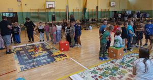 Dzieci grają w wielkoformatową grę planszową „Wygraj bezpieczeństwo”, pokazującą, jak działa grywalizacja w edukacji o zasadach ruchu drogowego.