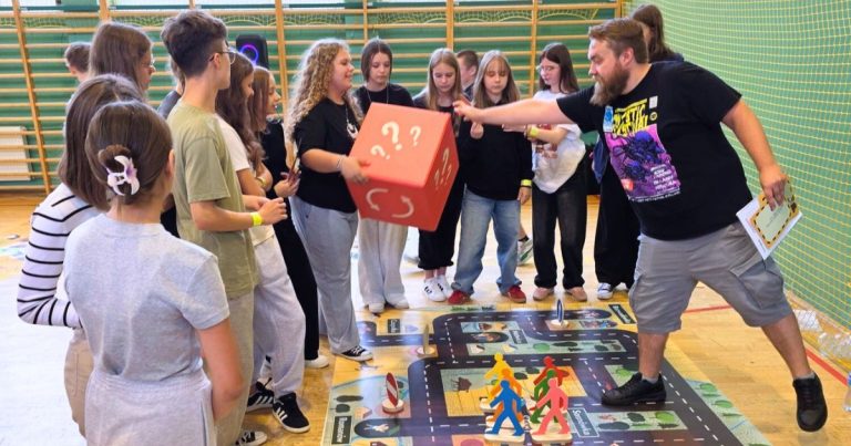 Dzieci grają w wielkoformatową grę planszową „Wygraj bezpieczeństwo”, pokazującą, jak działa grywalizacja w edukacji o zasadach ruchu drogowego.